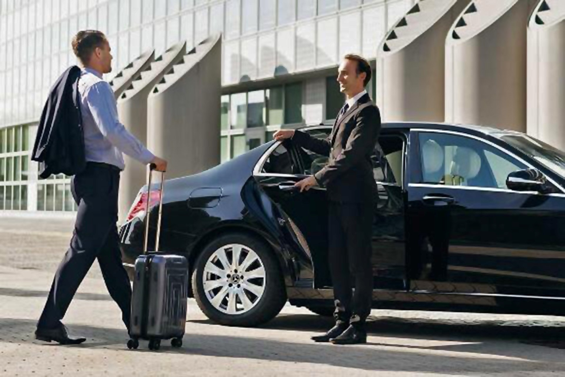 Blogs 13 Professional Frisco chauffeur service assisting a business traveler with luggage beside a luxury black sedan outside a modern building.