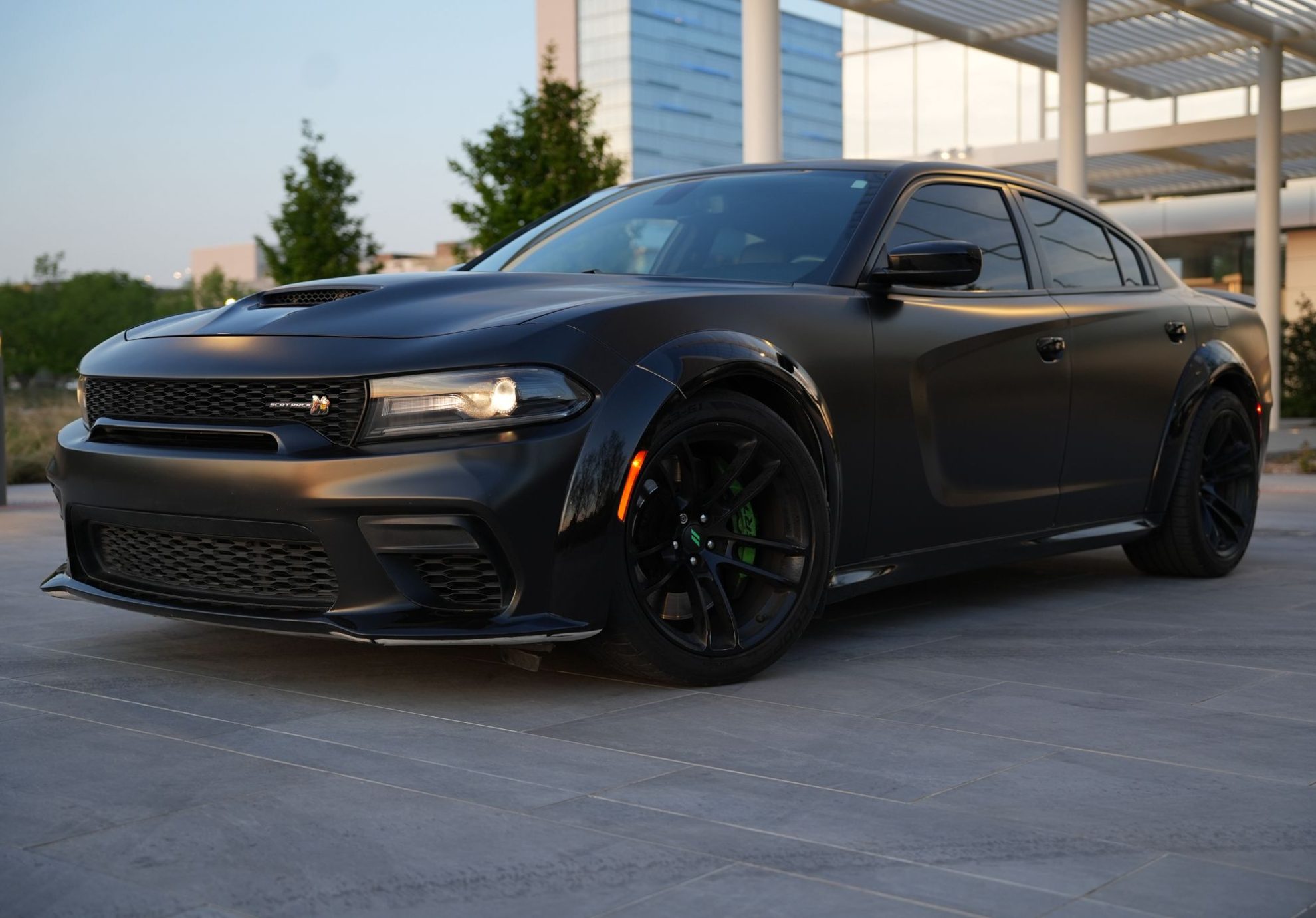 Dodge Charger Scat Pack Rental Dallas with black rims and green brake calipers parked outside modern architecture